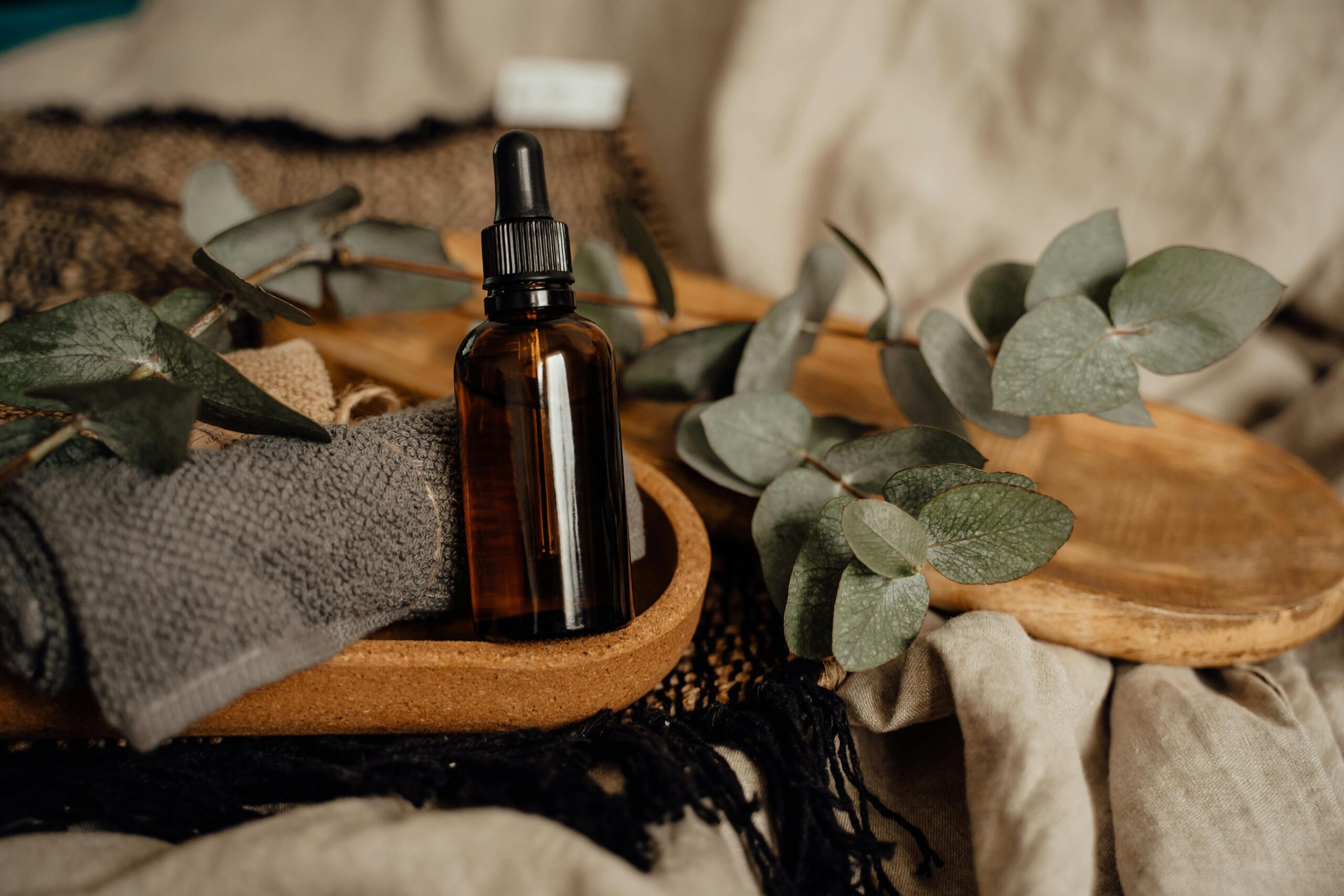 Still life of an amber glass bottle with eucalyptus and towel on a wooden tray.